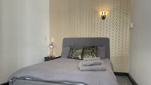A neatly made bed with a grey duvet and pillows, a bedside lamp, and a wall-mounted light fixture. - Burne Jones By LFD (Birmingham)