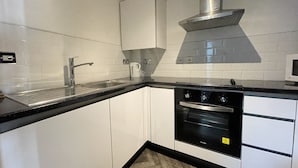 A modern kitchen with white cabinets, a black countertop, stainless steel appliances, and a microwave. - Burne Jones By LFD (Birmingham)