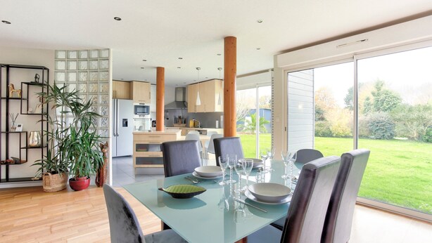 A modern dining area with a glass table, chairs, and a view of the garden.