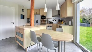A modern kitchen with a central island, white chairs, and pendant lights.