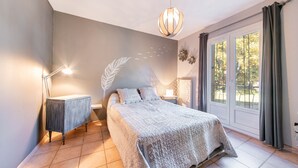 Ein Schlafzimmer mit Bett, Nachttischlampen, einem Nachttisch, einem Wandbild und einem großen Fenster mit Vorhängen.