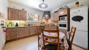 Eine Küche mit Holzausstattung, einem Esstisch mit Blumenmuster bedeckter Tischdecke, einem Kühlschrank mit Magneten und einer Pendelleuchte.