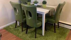 Ein Essbereich mit einem weißen Tisch und vier grünen Stühlen mit ovalen Rückenlehnen. Auf dem Tisch stehen drei kleine Topfpflanzen.