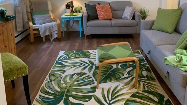 Ein Wohnzimmer mit einer Couch, Sesseln, einem Couchtisch, einem gemusterten Teppich und einer Lampe.