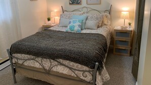 Ein ordentlich eingerichtetes Schlafzimmer mit einem Bett, zwei Nachttischen, einer Lampe und gerahmten Kunstwerken an der Wand.
