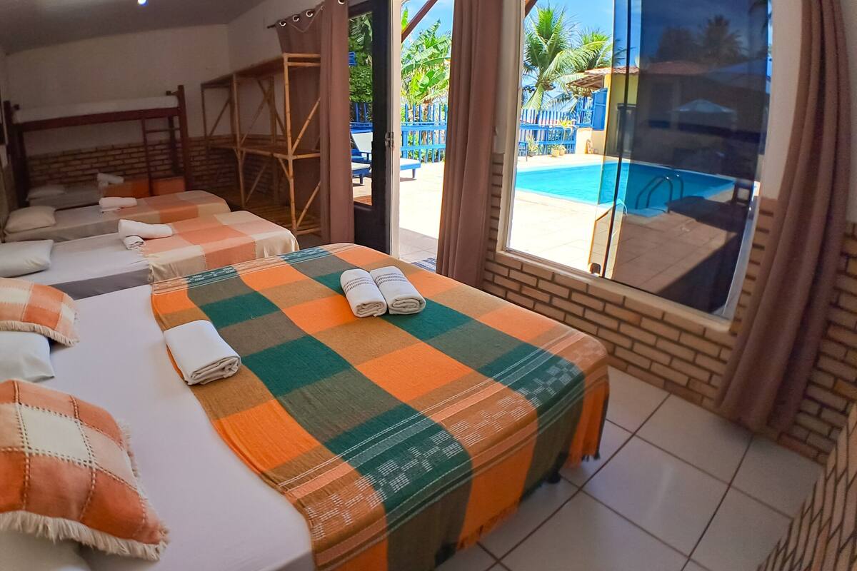 Une chambre d’hôtel avec une couvre-lit à carreaux, plusieurs oreillers, une vue sur la piscine et un balcon.