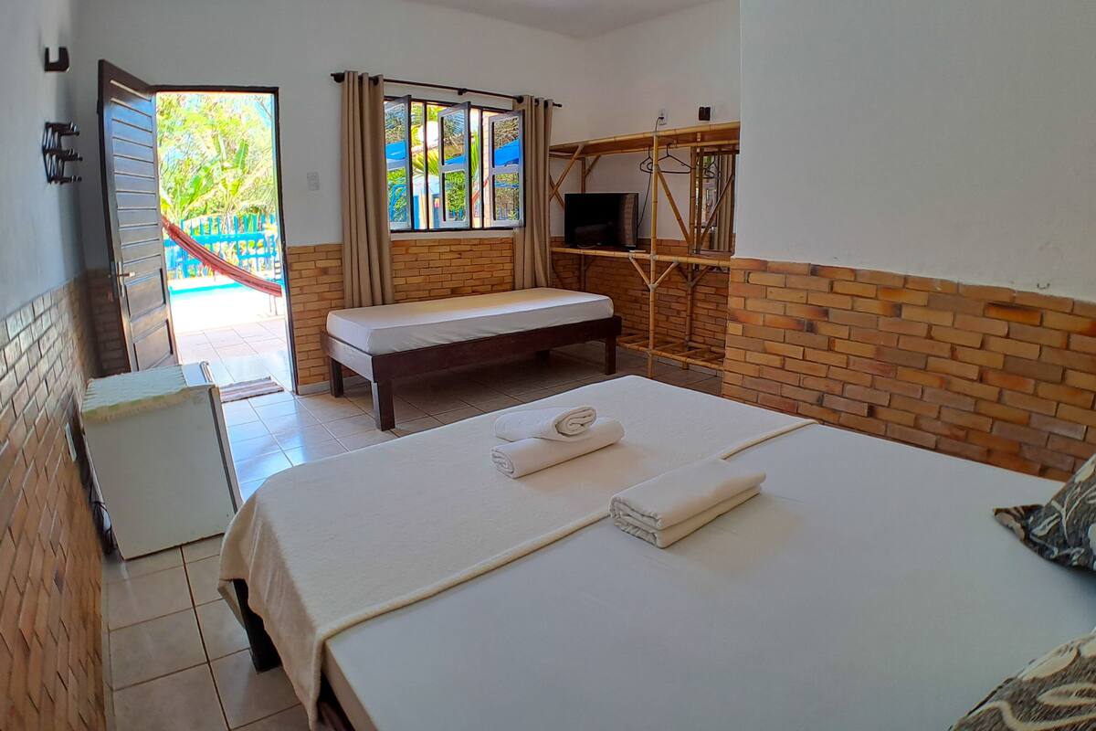 Une chambre d’hôtel avec un lit, un banc, une télévision et une vue sur une piscine.