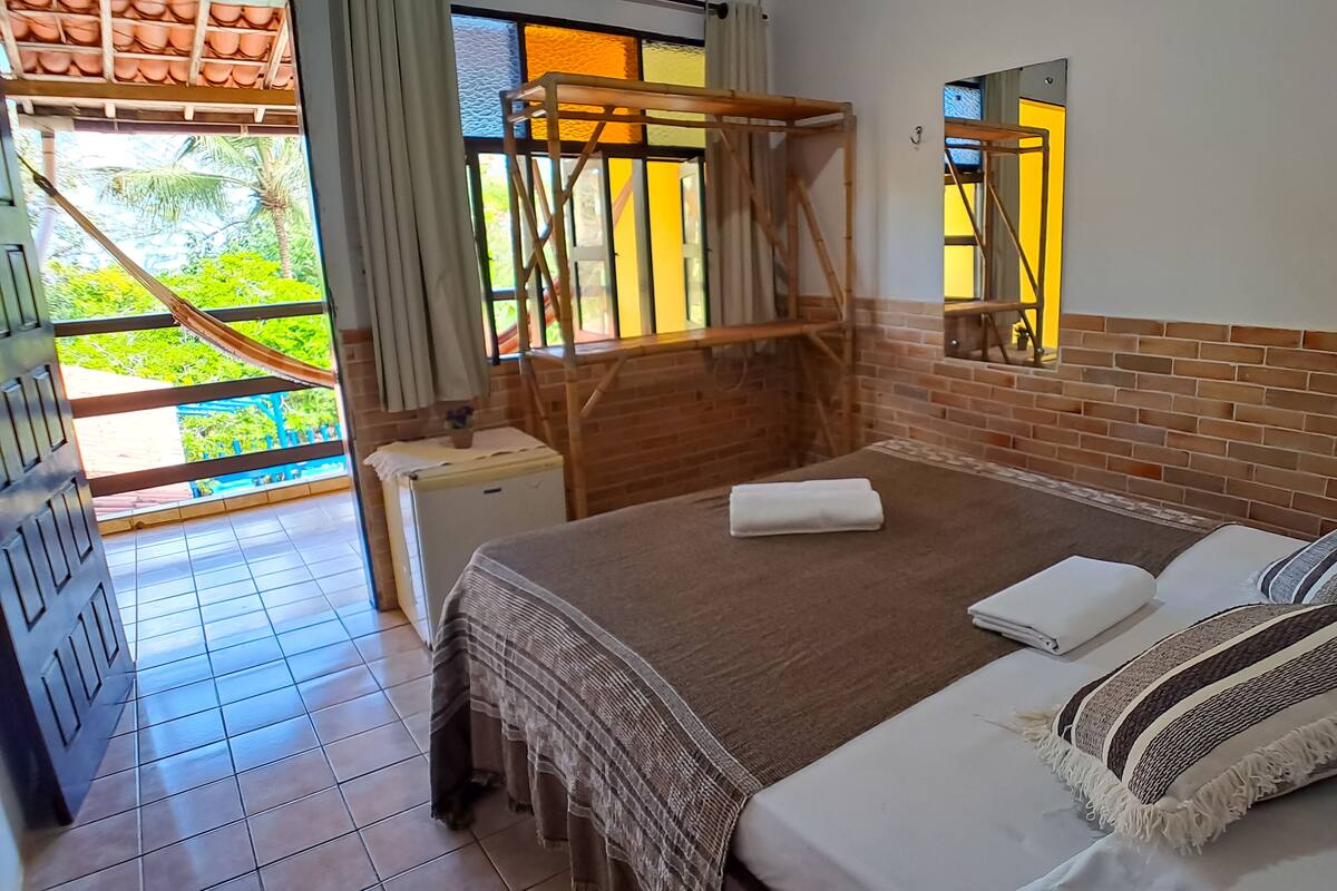 Une chambre d’hôtel avec un lit, une petite table, une fenêtre donnant sur un espace verdoyant et un mur en briques.