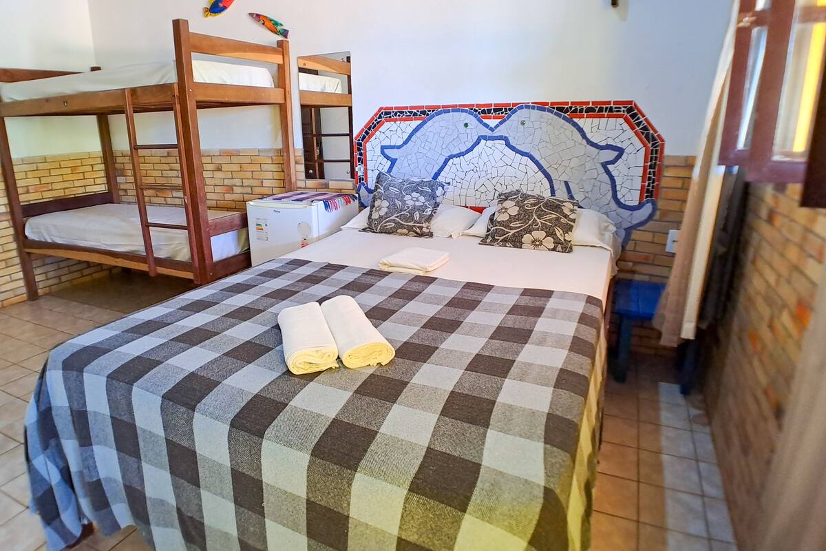 Une chambre avec une couvre-lit à carreaux, deux lits superposés, un réfrigérateur et un mur orné d’une mosaïque.