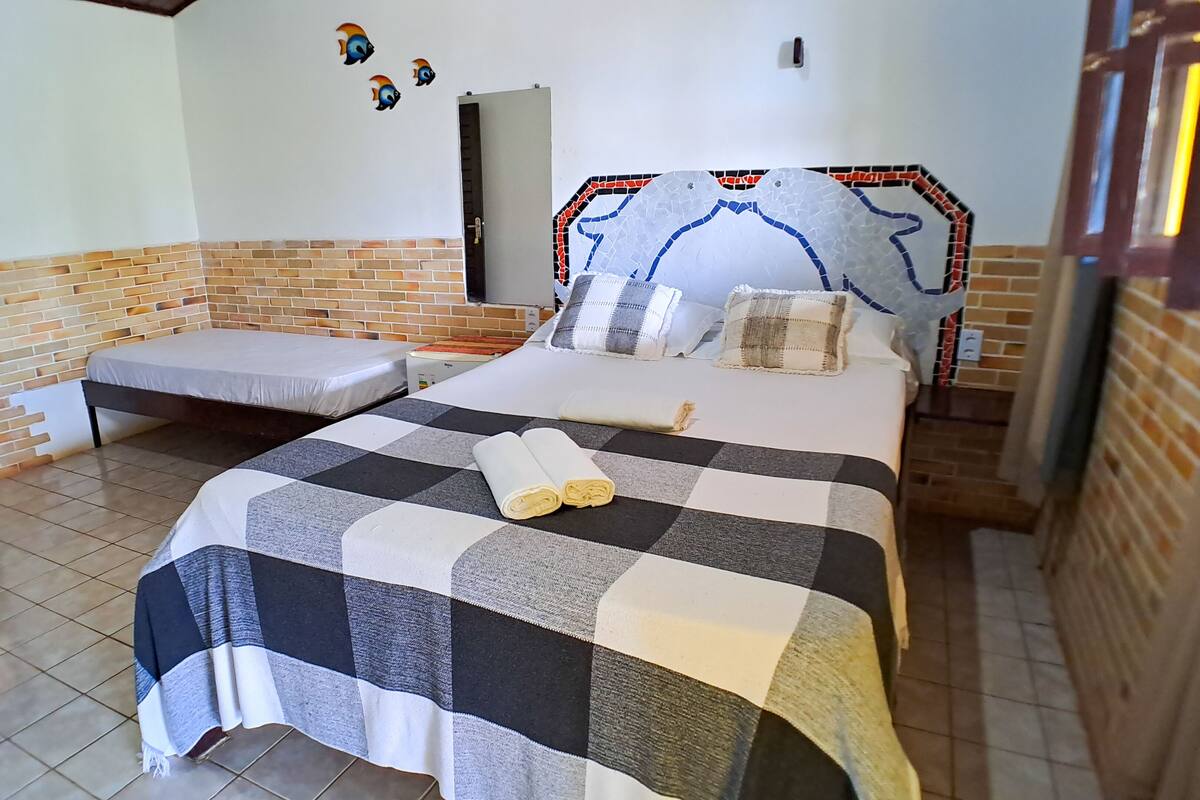 Une chambre à coucher avec une couvre-lit à carreaux, un lit simple, un banc attenant et un sol carrelé.