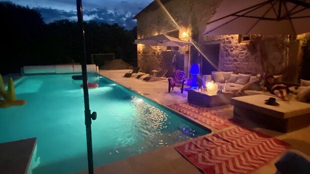 Zona de piscina con jacuzzi, sillas de descanso y un muro de piedra al fondo.