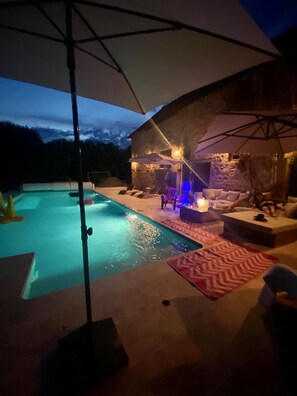Un espace piscine doté d’un jacuzzi, de chaises longues et d’un mur en pierre servant de décor.