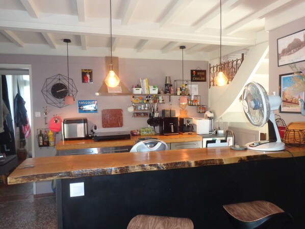 Un espace bar doté d’un comptoir en bois, de tabourets de bar, de luminaires suspendus et de divers appareils de cuisine.