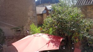 Un paraguas rojo, una silla de madera y un árbol con flores moradas.