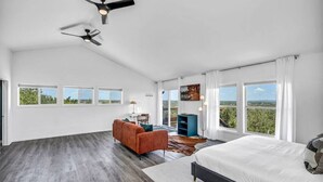A spacious bedroom with a large bed, a sofa, and a desk. There are multiple windows providing a view of the outdoors.