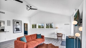A spacious living room with a large window, a ceiling fan, a sofa, a coffee table, and a rug.