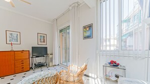 Una habitación luminosa con televisión, sillas de mimbre, una mesita con un cuenco de flores y una cama.