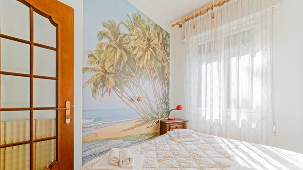 Un dormitorio con un mural de playa, una cama con colcha floral y una mesita de noche con lámpara.