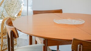 Una mesa redonda de madera con un plato blanco en el centro, rodeada de sillas de mimbre con asientos acolchados.