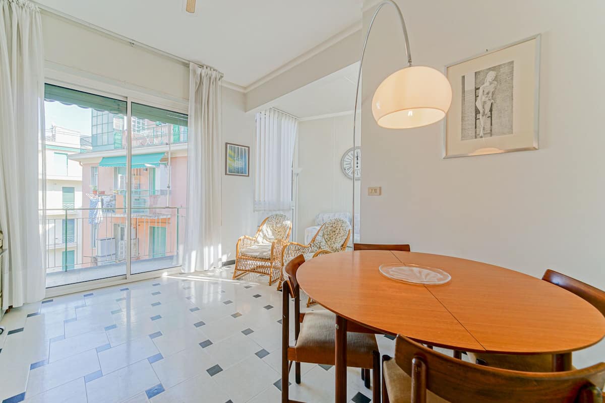 A spacious dining area with a wooden table and chairs, a large window with a view of buildings, and a ceiling light fixture.