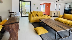 Een moderne woonkamer met een gele bank, een houten salontafel en een eettafel.