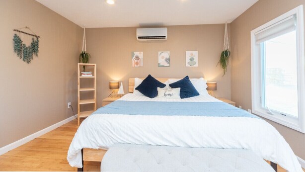 A bedroom with a bed, bedside tables, a ceiling fan, wall-mounted air conditioning, and a window. - Cozy Boston Homestead : Sleeps 8, Pet Friendly (Framingham)
