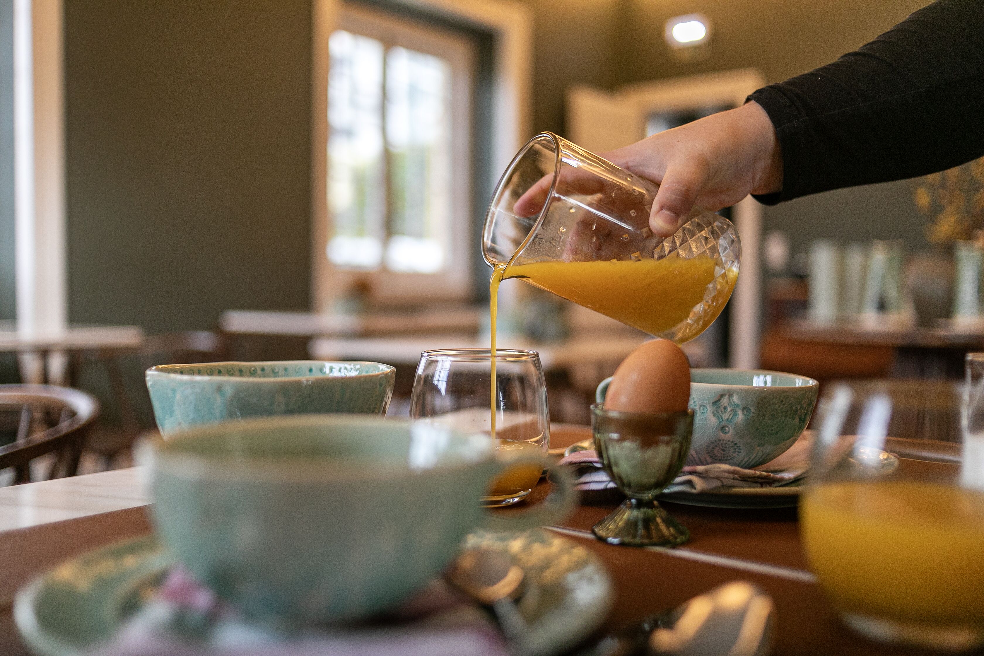 A hand pouring orange juice into a glass.