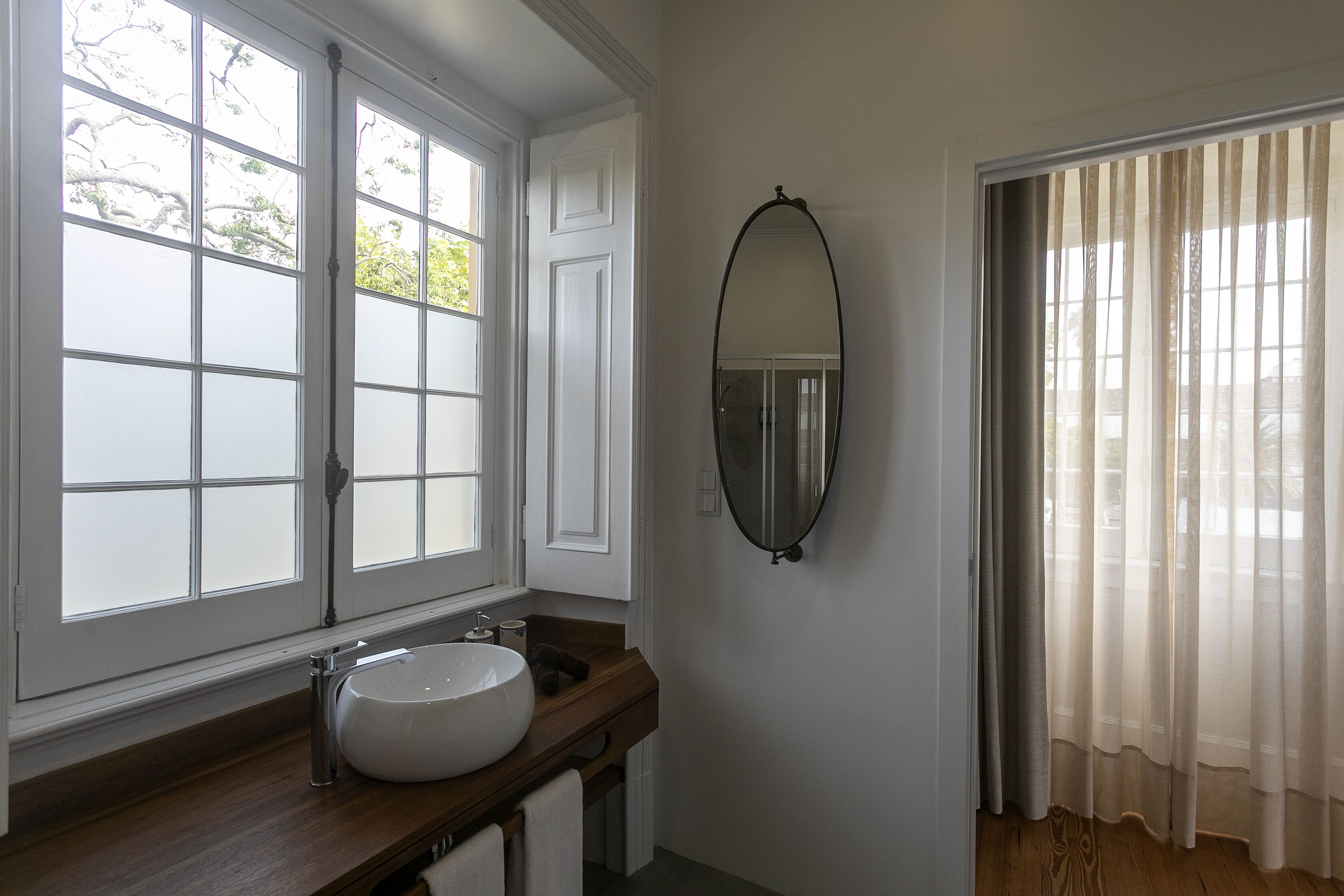 A bathroom with a large window, a wooden vanity, a white sink, and a mirror.