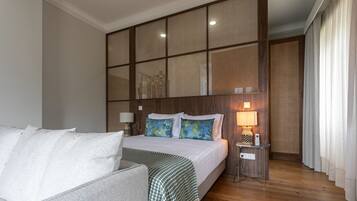 Une chambre d’hôtel avec un lit, une table de chevet avec une lampe, une tête de lit en bois et une vue sur l’extérieur par une fenêtre avec des rideaux.