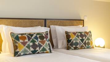 Habitación de hotel con una cama con ropa blanca y dos almohadas decorativas de estampado geométrico.
