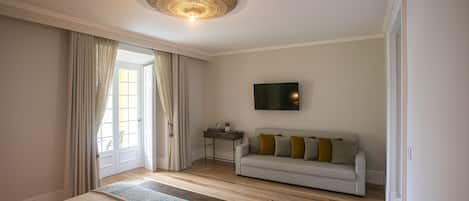A bedroom with a bed, a sofa, a TV, and a door leading to a balcony.