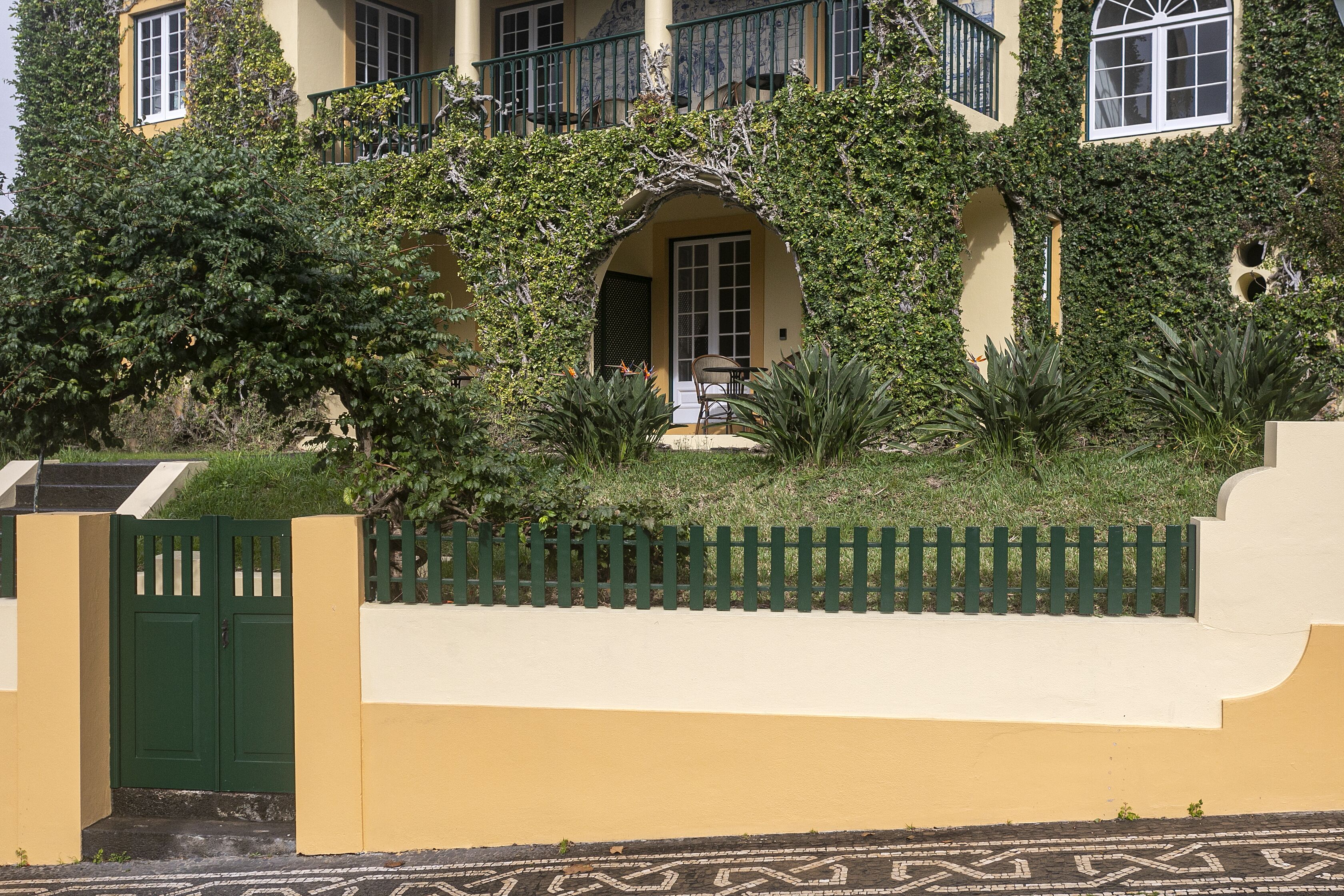 A building with a yellow facade, green gate, and a patterned floor.