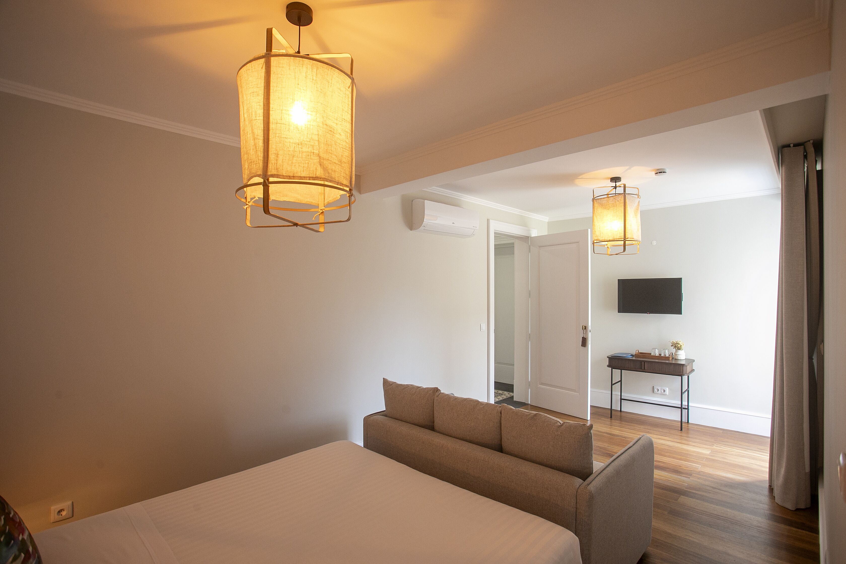 Ein Hotelzimmer mit Bett, Sofa, zwei Pendelleuchten, einem Flachbildfernseher und einem kleinen Tisch.
