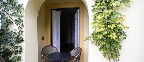 An outdoor seating area with a round table and two chairs, an archway, and climbing plants on a wall.