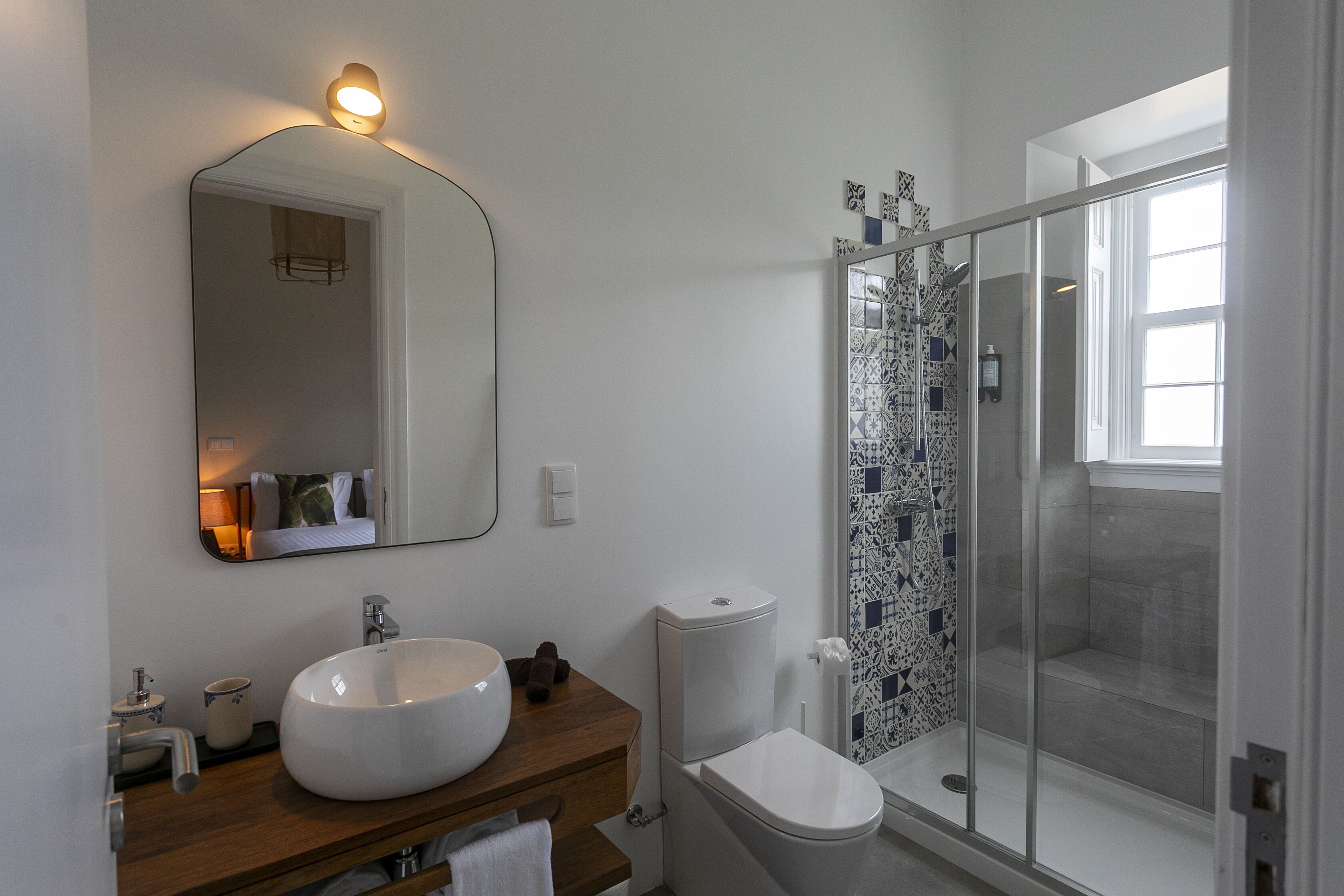 A modern bathroom with a large white sink, a mirror, a toilet, and a glass-enclosed shower.