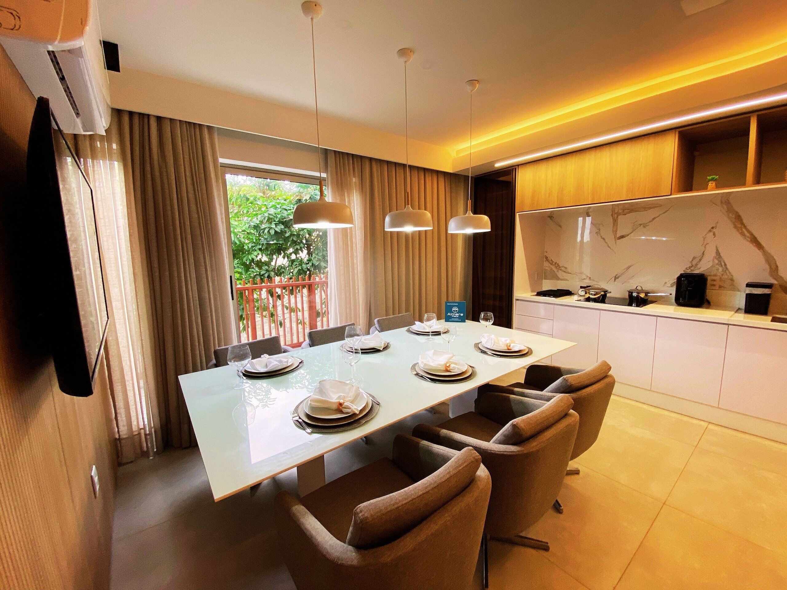 A modern dining area with a long table, multiple chairs, and pendant lighting.