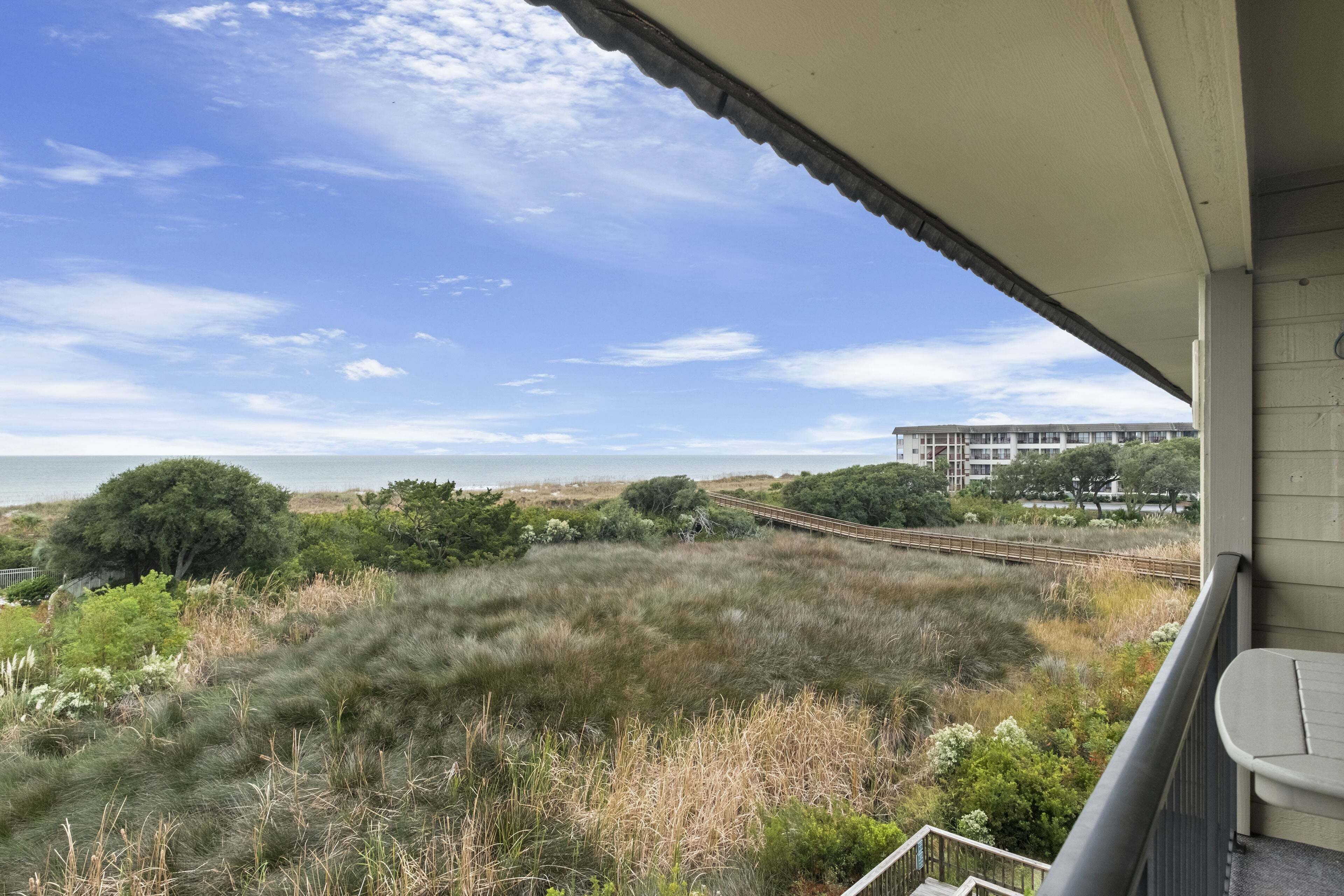 A balcony with a view of a coastal landscape, including a grassy area, trees, and a distant building.
