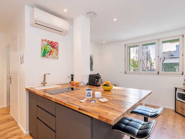 A modern kitchen with a wooden island, a coffee machine, and a bowl of fruit.