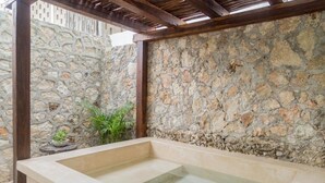 A stone-walled outdoor spa area with a rectangular hot tub. - Hotel Maculan (Valladolid)