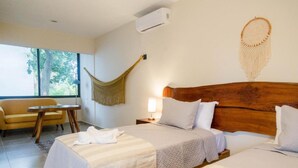 A hotel room with a large bed, a smaller bed, a hammock, a sofa, and a window with a view of trees. - Hotel Maculan (Valladolid)