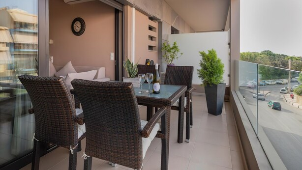 Un balcon avec des fauteuils en osier, une table avec des verres à vin, une plante en pot et une vue sur la rue.