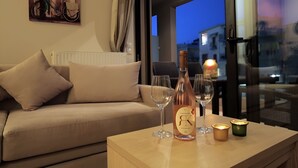 Un salon chaleureux avec un canapé, une table sur laquelle se trouvent une bouteille et des verres, et une vue sur la ville au crépuscule.