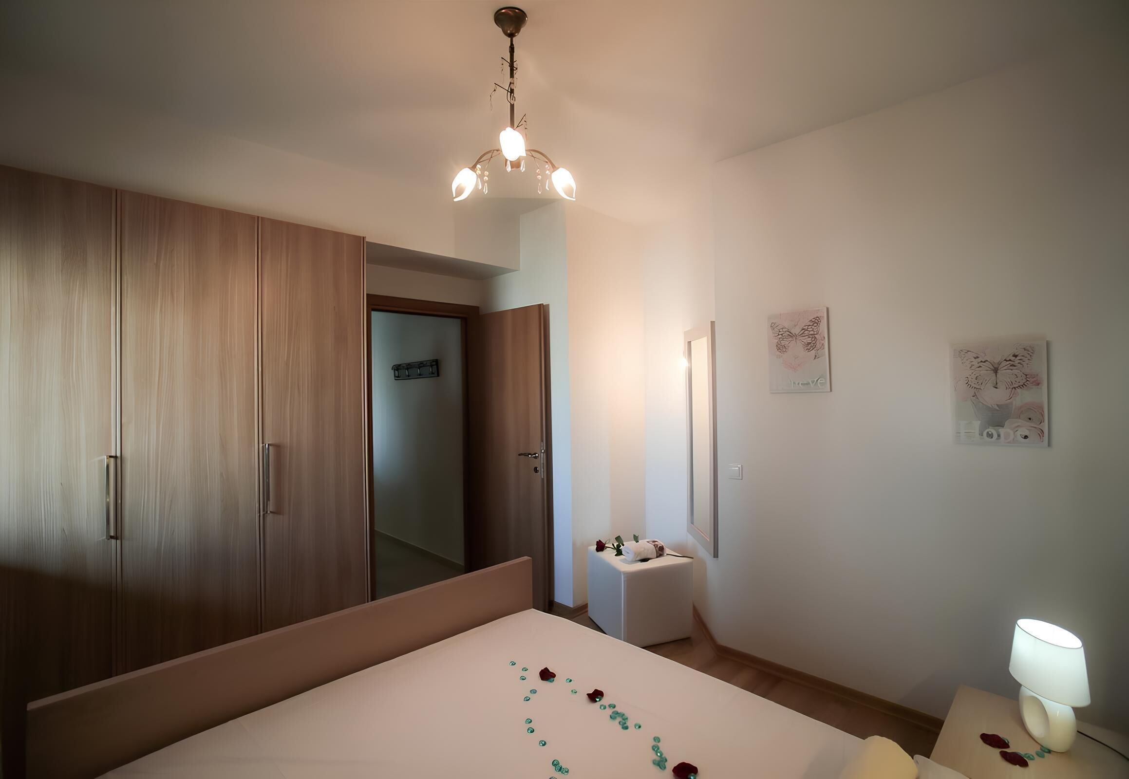 A bedroom with a bed, a wardrobe, a bedside table with a lamp, and a small bedside table with a decorative item.