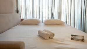 Un lit bien fait, avec des draps blancs, deux oreillers et des serviettes enroulées. Un livre est posé sur le lit.