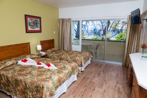 A hotel room with two beds, a TV, a balcony with a view of trees and a body of water, and a painting on the wall.