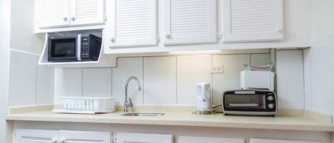 A kitchen with white cabinets, a microwave, a toaster, and a sink.