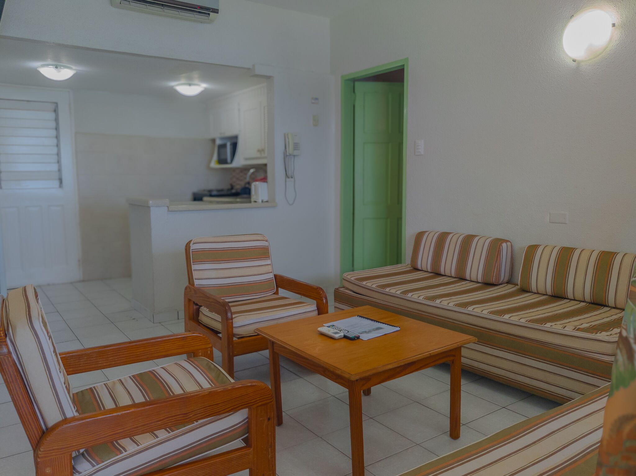 A small, clean room with a sofa, two striped chairs, a wooden table, and a green door.