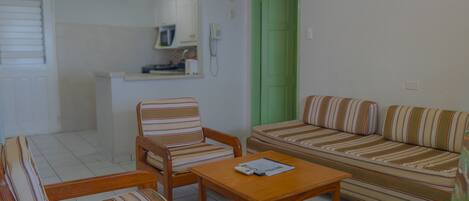 A small, clean room with a sofa, two striped chairs, a wooden table, and a green door.