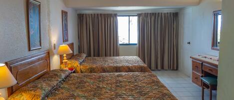 A hotel room with two beds, a desk, and a window with curtains.
