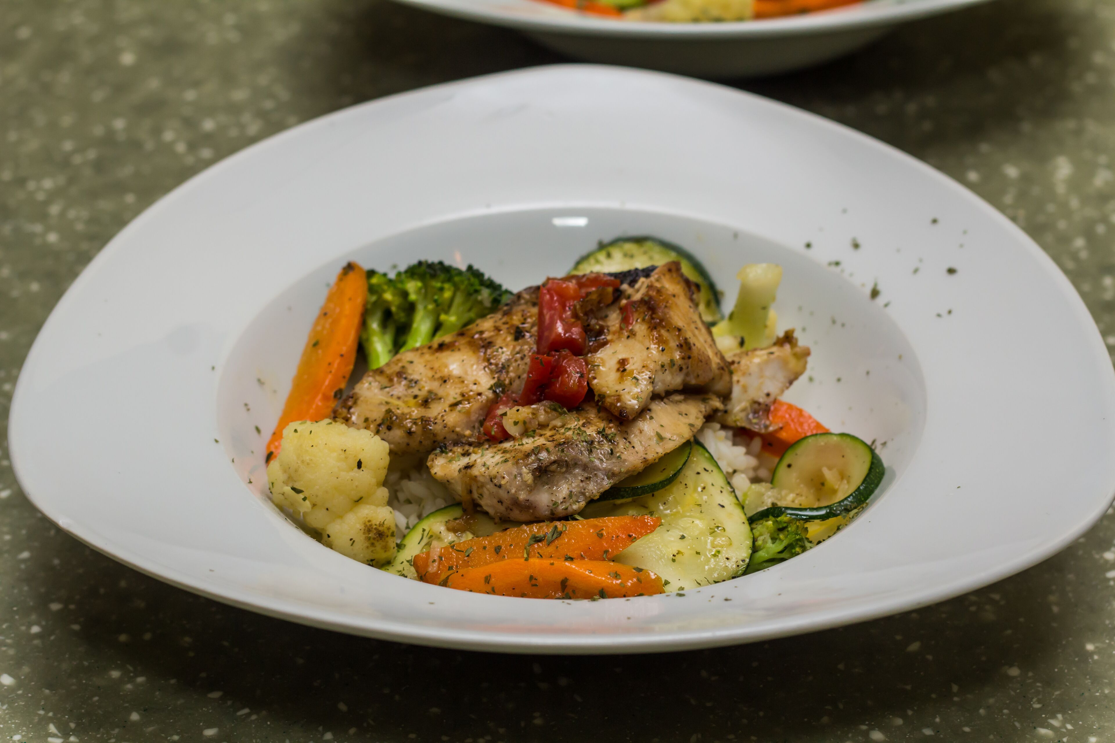 Une assiette de nourriture composée de poulet, de légumes et de riz.